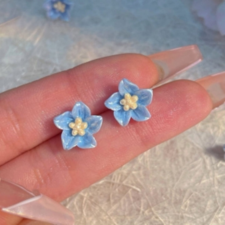 De oorbellen van de blauwe bloemenstudie zijn delicaat en klein
