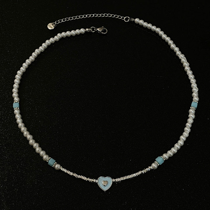 Corazón amante de azul que cose pequeños piezas de collar de perlas de plata