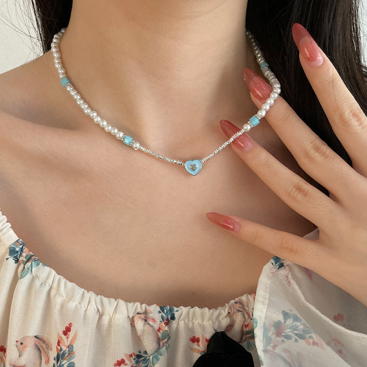 Corazón amante de azul que cose pequeños piezas de collar de perlas de plata