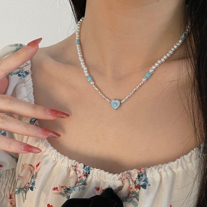 Corazón amante de azul que cose pequeños piezas de collar de perlas de plata